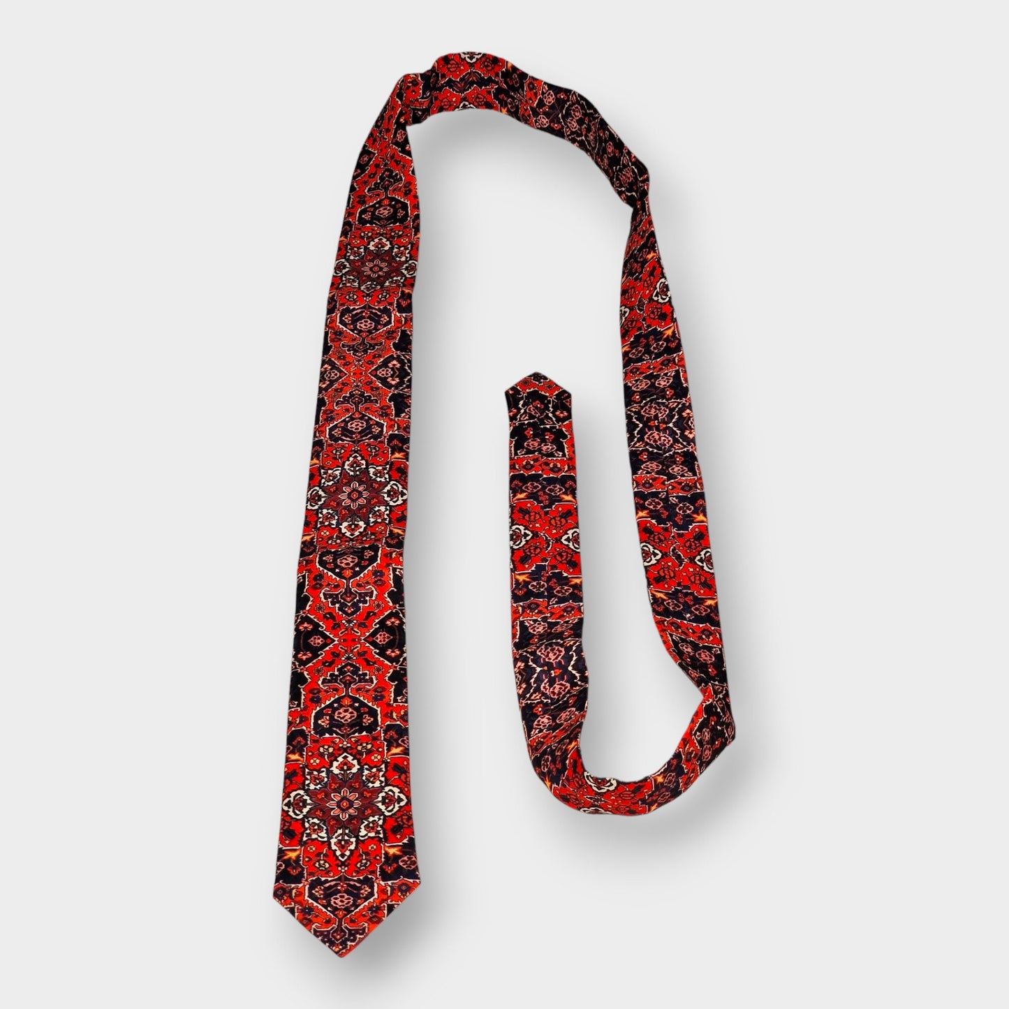 Corbata de crepé de seda inspirada en los diseños de las alfombras persas con motivos florales en tonalidades rojizas.